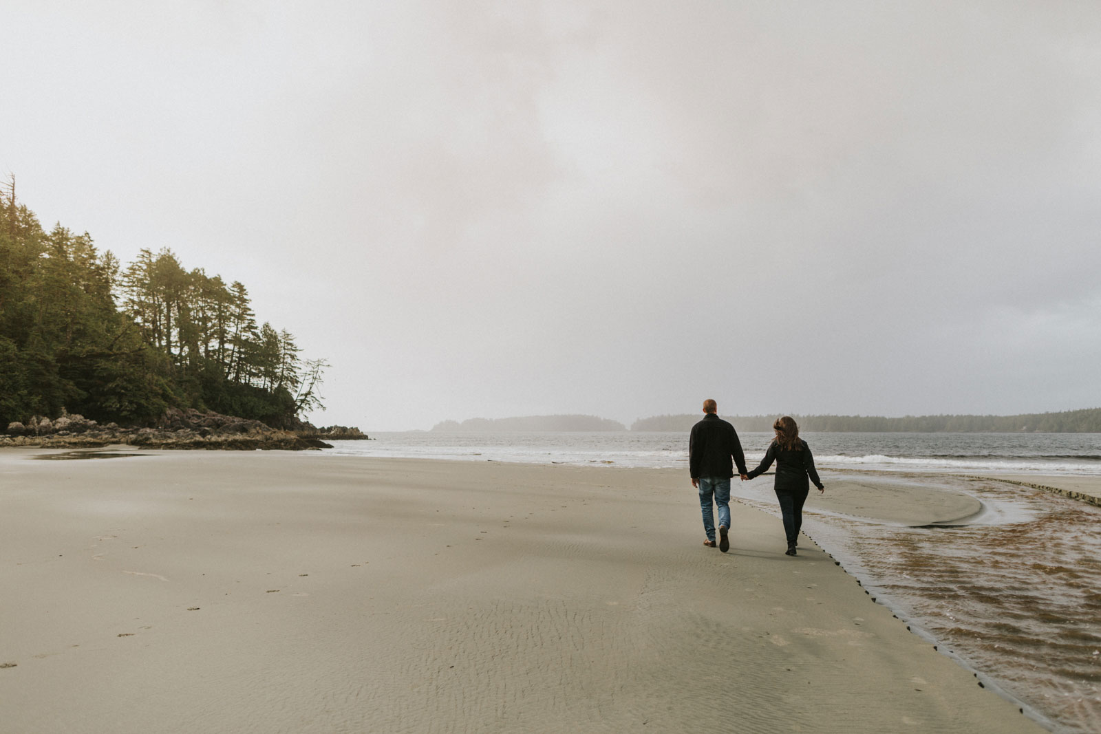 Couple holding hands and walking on the beach in Tofino BC