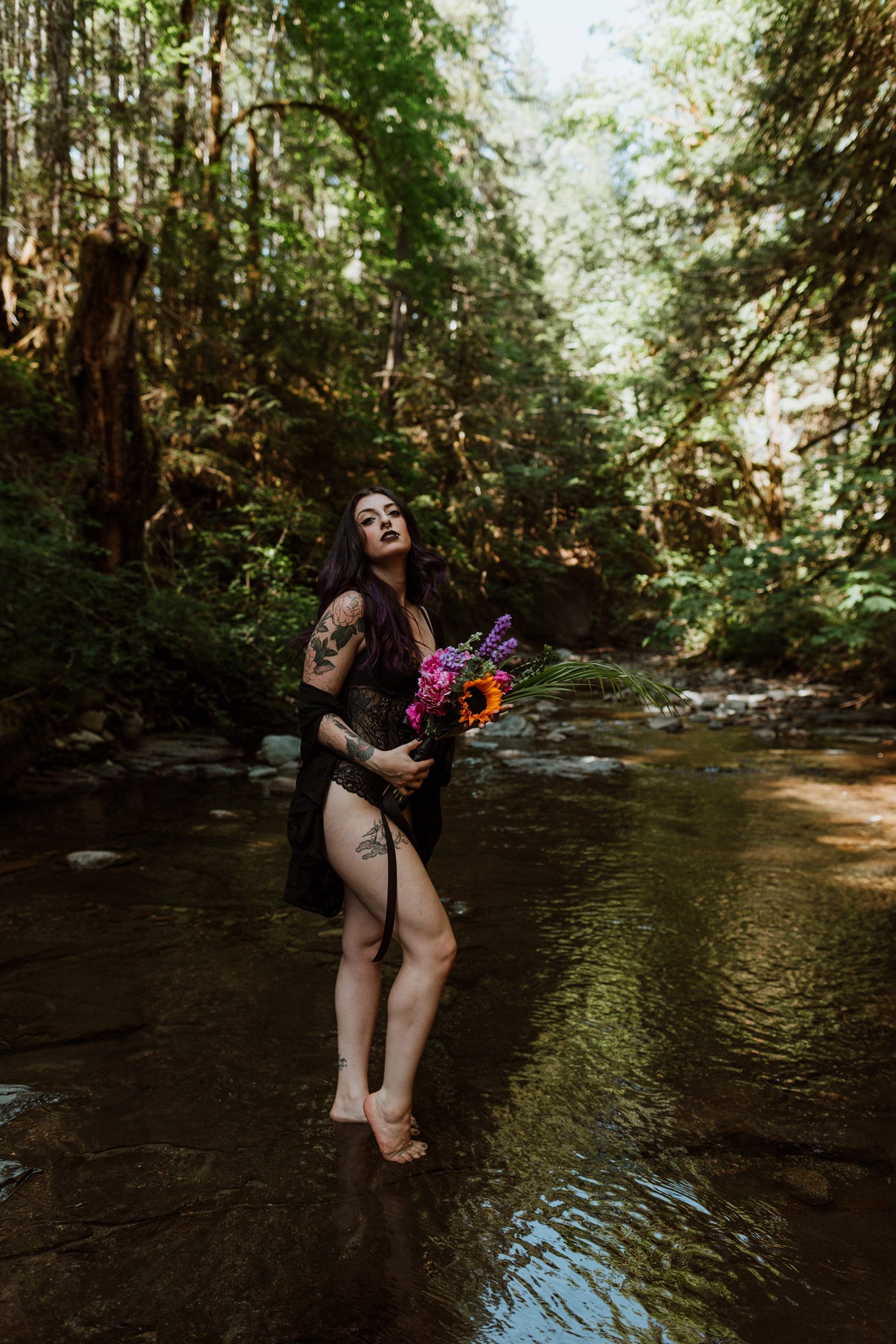Woman with tattoos standing in a creek with a bouquet