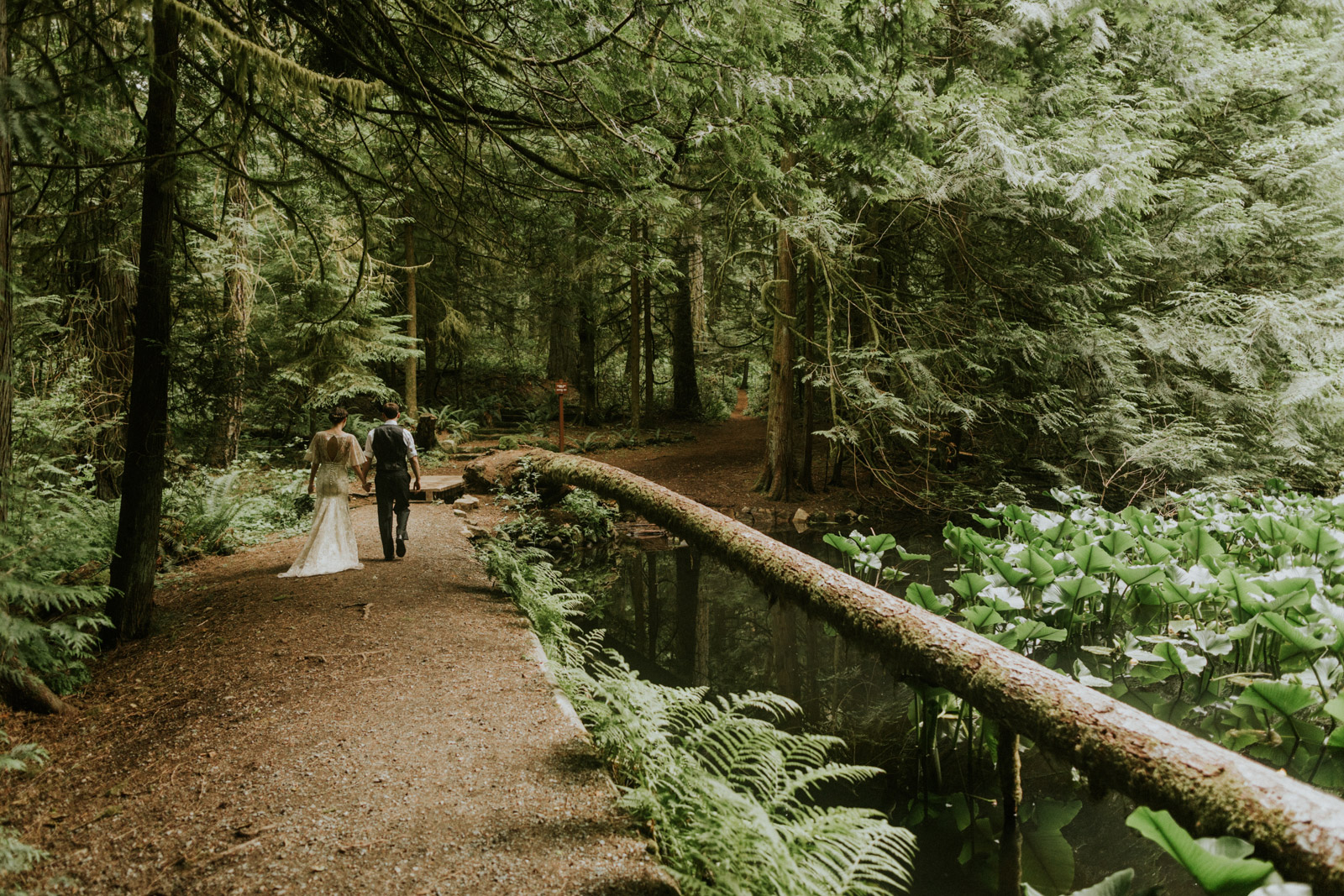 Bride and groom walking down a forest trail